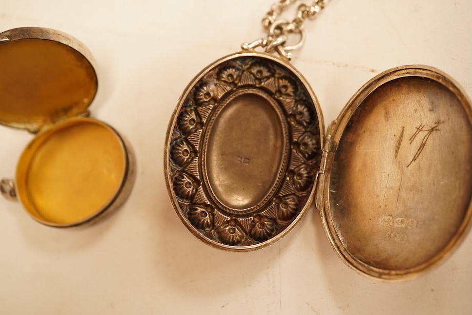 A late Victorian embossed and engraved oval silver locket, 42mm, on a later white meta belcher link chain, together with an Edwardian silver and hardstone inlaid pill box, now with pendant mount.